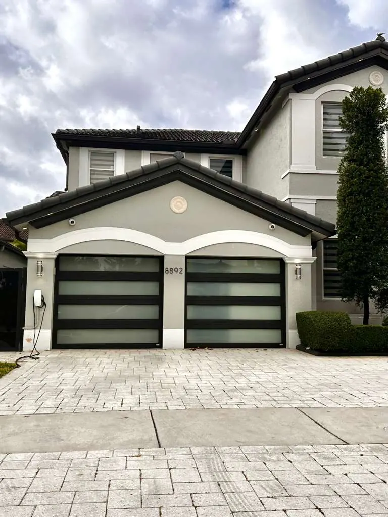 Two black-frame impact glass garage doors on a two-story Mediterranean-style home