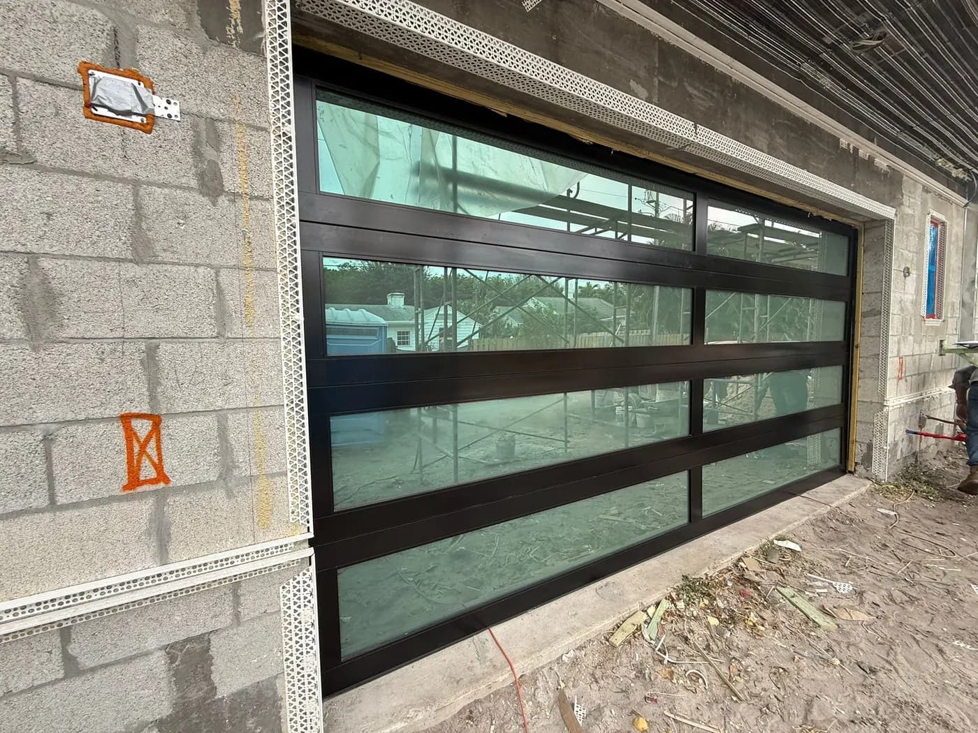 Black frame impact glass garage door being installed on a concrete block garage under construction
